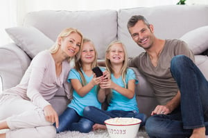 Twins and parents eating popcorn and watching television sitting on a carpet